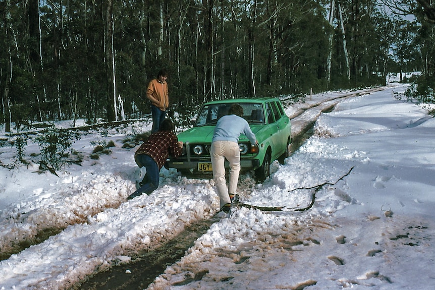 Men push an old fashioned Subaru stuck in the snow. 