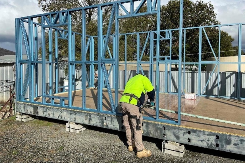 A tradesman assembling the frame of a bungalow in a back yard