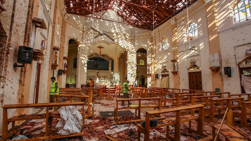 Three men inspect the inside of a church that was torn apart in a bombing, scattering debris across the floor and walls