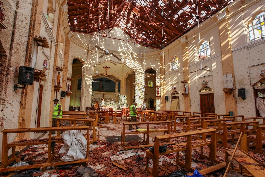 Three men inspect the inside of a church that was torn apart in a bombing, scattering debris across the floor and walls