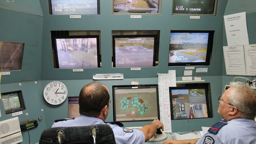 two men in uniforms sitting in a panel of CCTY monitors