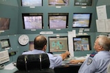 two men in uniforms sitting in a panel of CCTY monitors