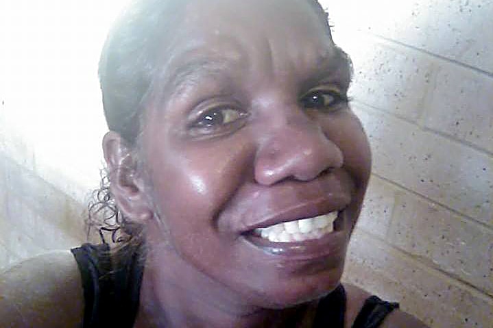 A young woman takes a smiling selfie wearing a black singlet.