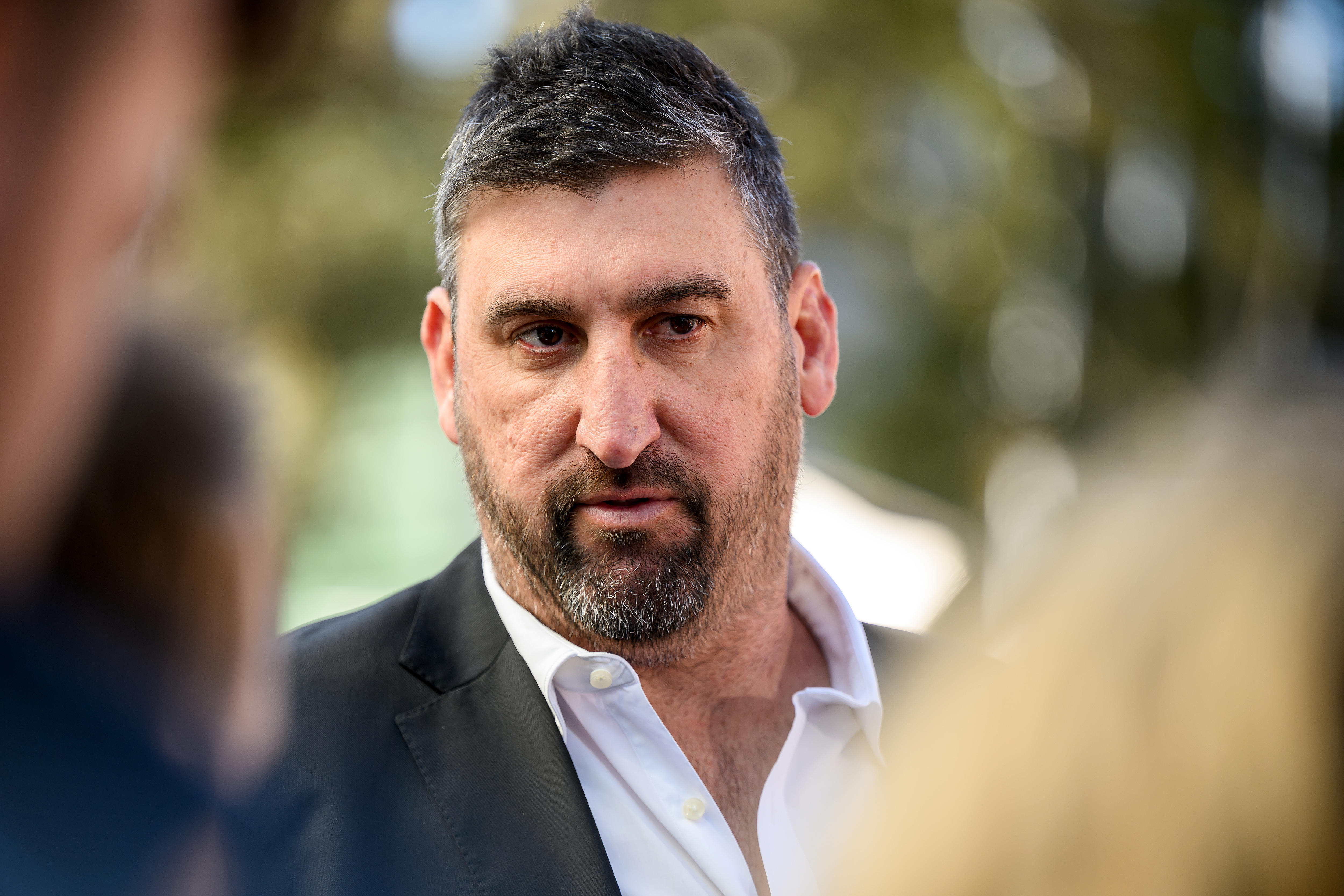 A man in a suit walks through a group of reporters.