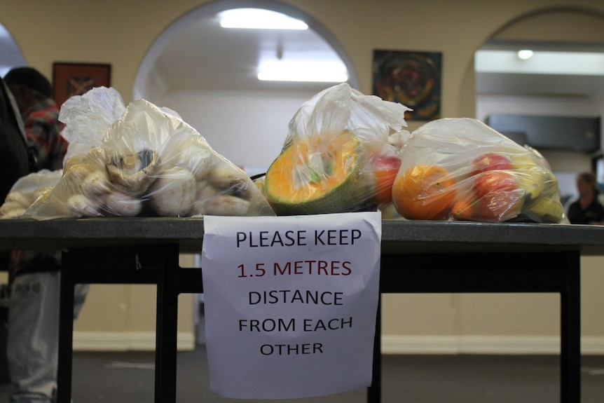 bags of fruit on top of table with sign telling people to observe social distancing