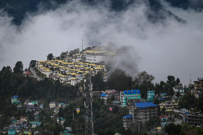 A sprawling monastery sits on top of a hill, covered by clouds