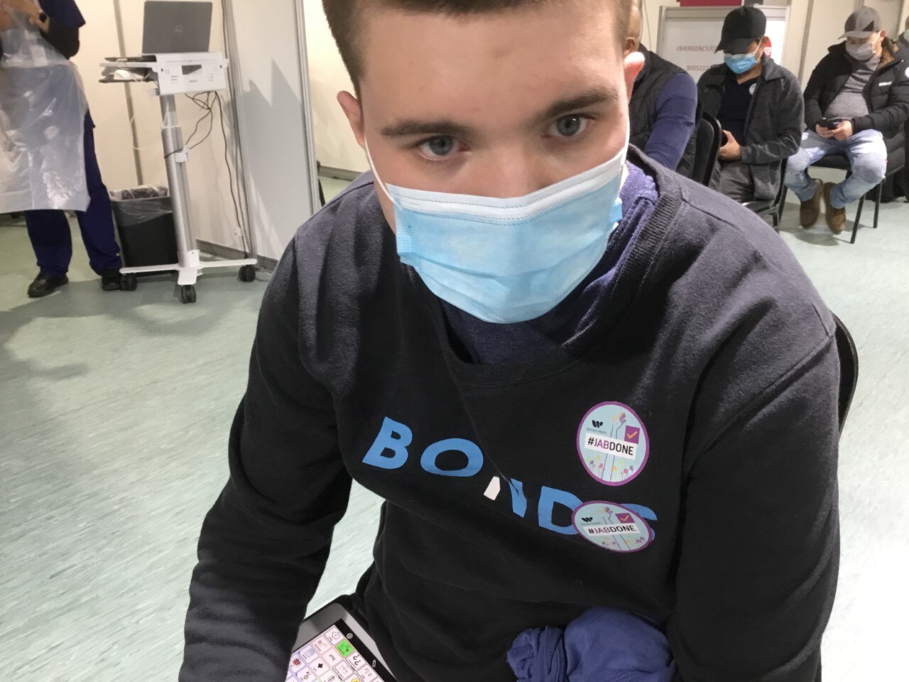 Boy in blue medical mask and black top looks at camera.