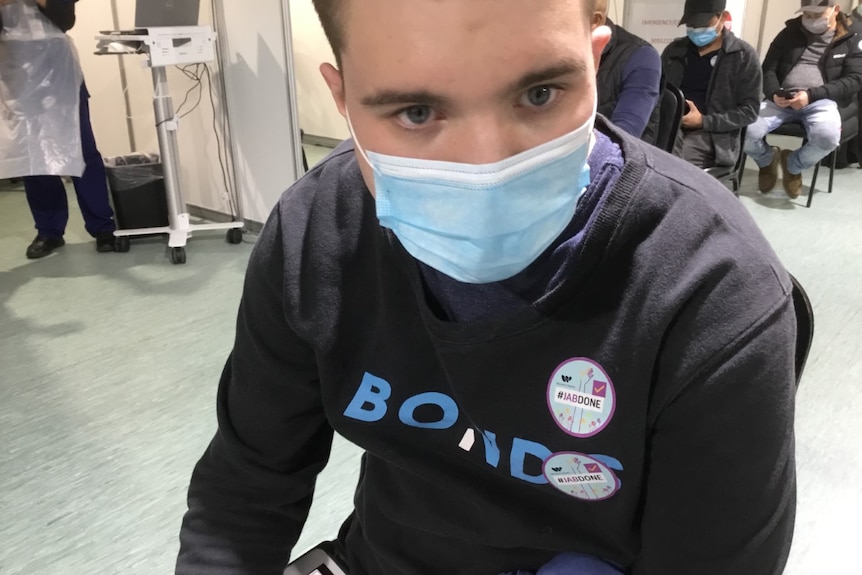 Boy in blue medical mask and black top looks at camera.