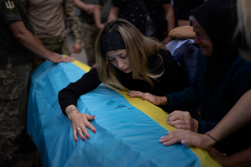 A woman cries over the coffin of her husband which is draped in the Ukrainian flag