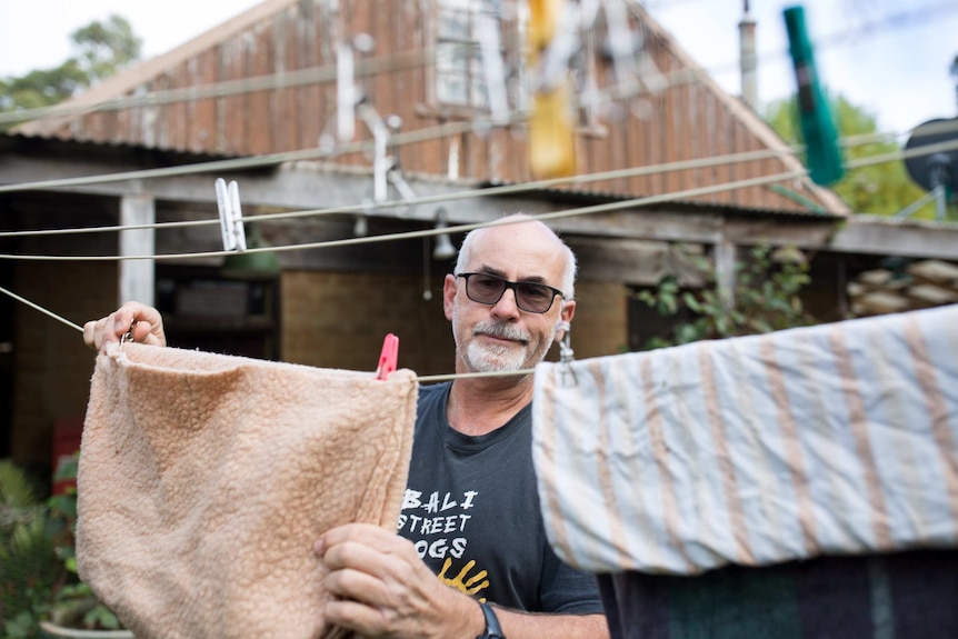 Manfred Zabinskas pegs pouches on the clothes line, his old barn-like house in the background.