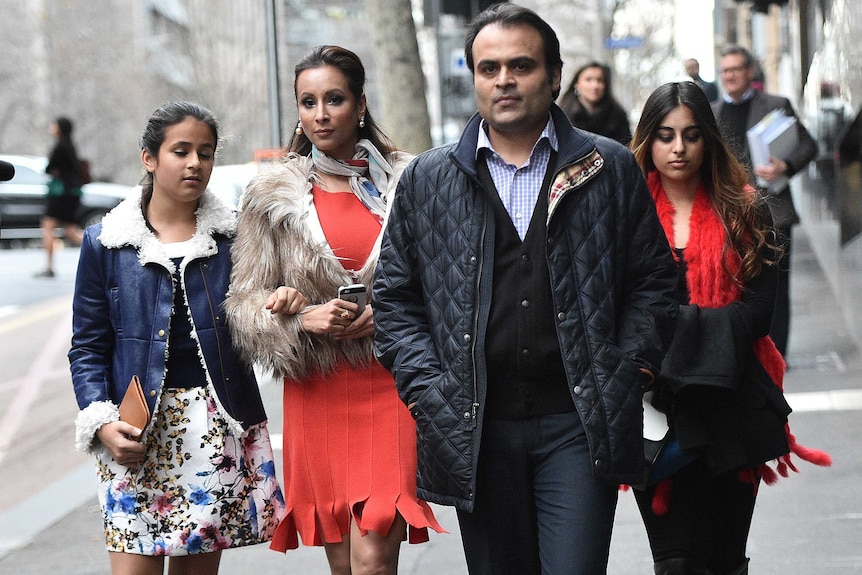 Panjak and Radhika Oswal walk along the footpath towards a camera with their two daughters.