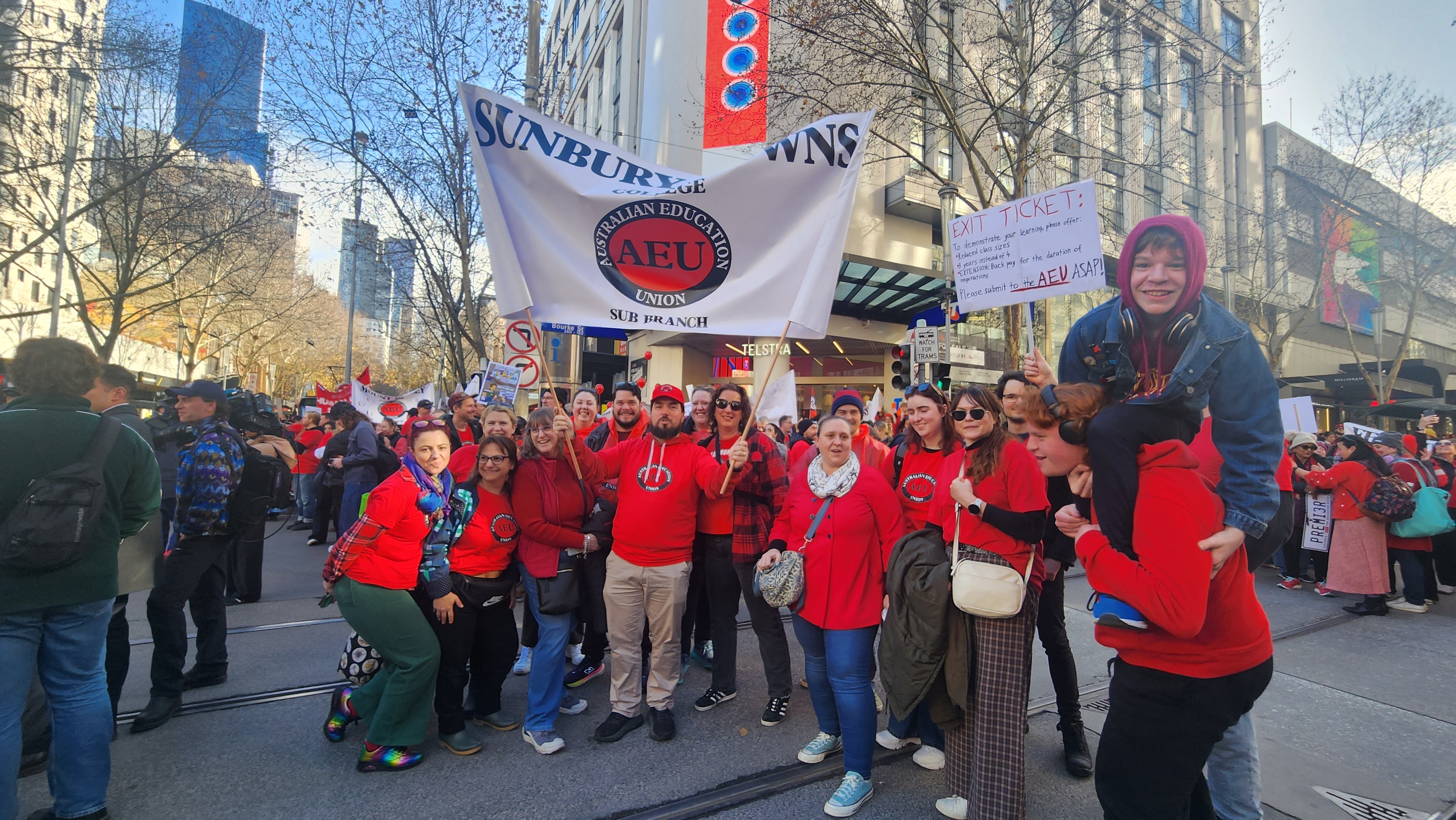 A group of people dressed in red hold Victorian Teachers' Union banners.