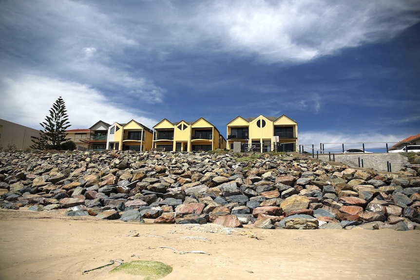 The beach at Somerton Park in Adelaide with houses behind a rocky shore and sand.