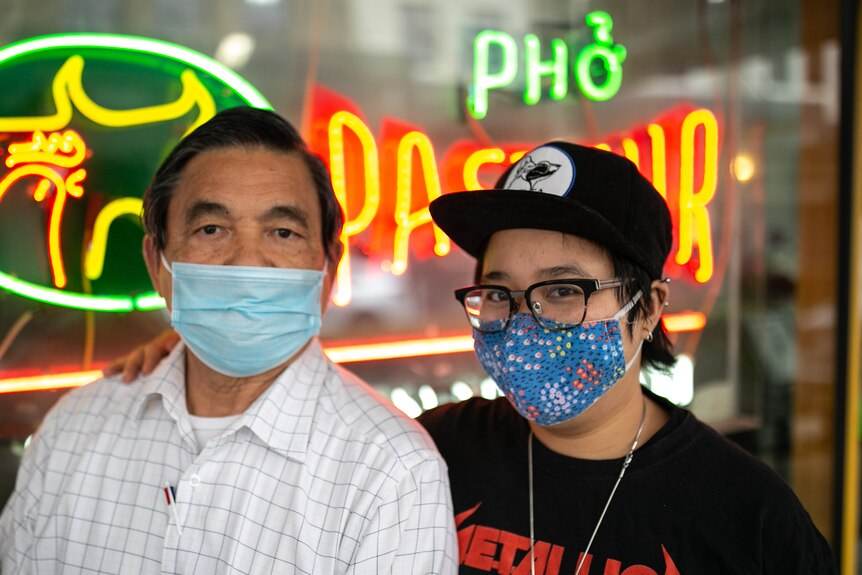 A man and a young woman stand in front of the sign of a Vietnamese restaurant. 