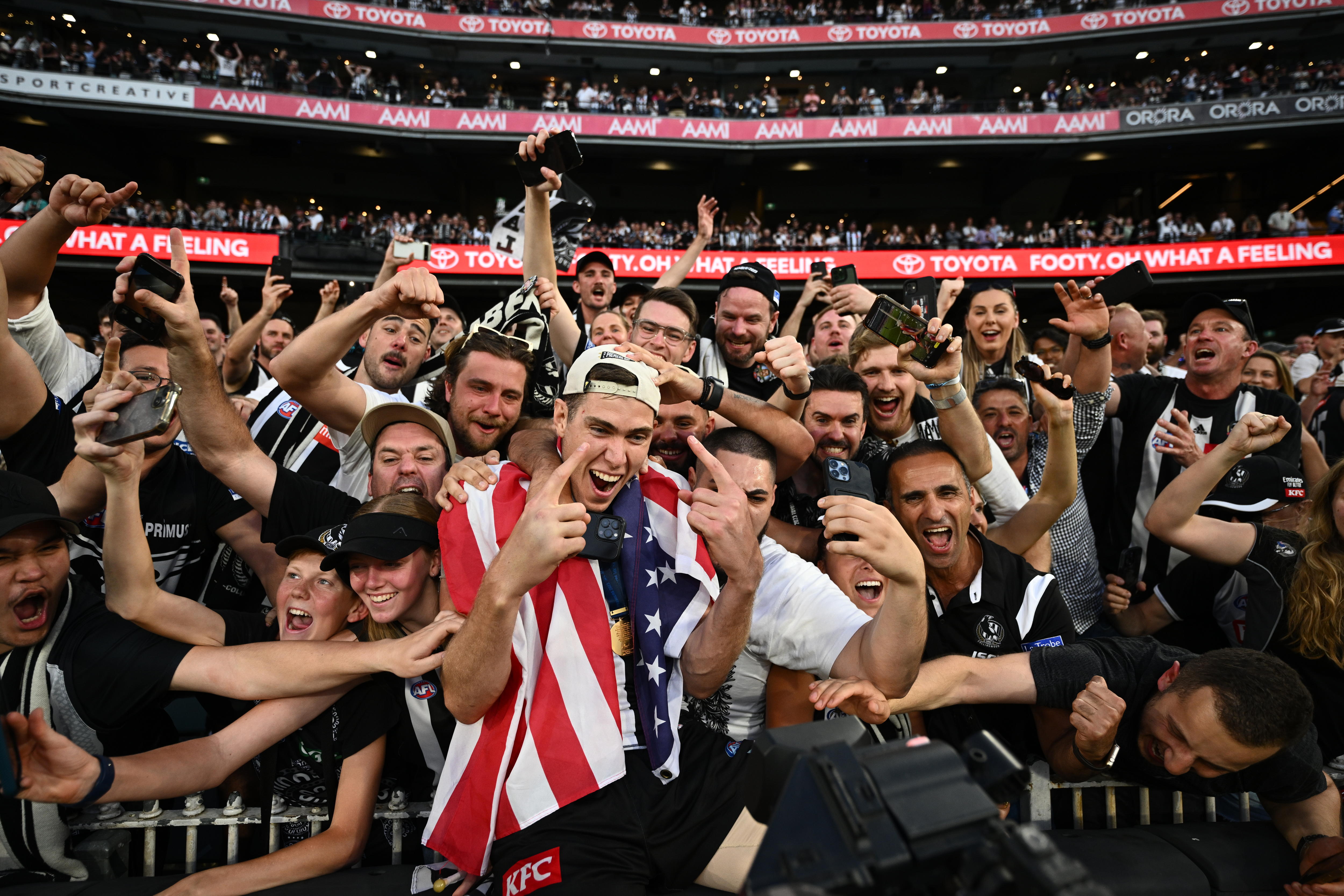 Mason Cox celebrates with Collingwood fans, wearing a US flag.