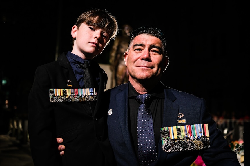 Peter and Talon smile, wearing medals, shrouded by darkness.