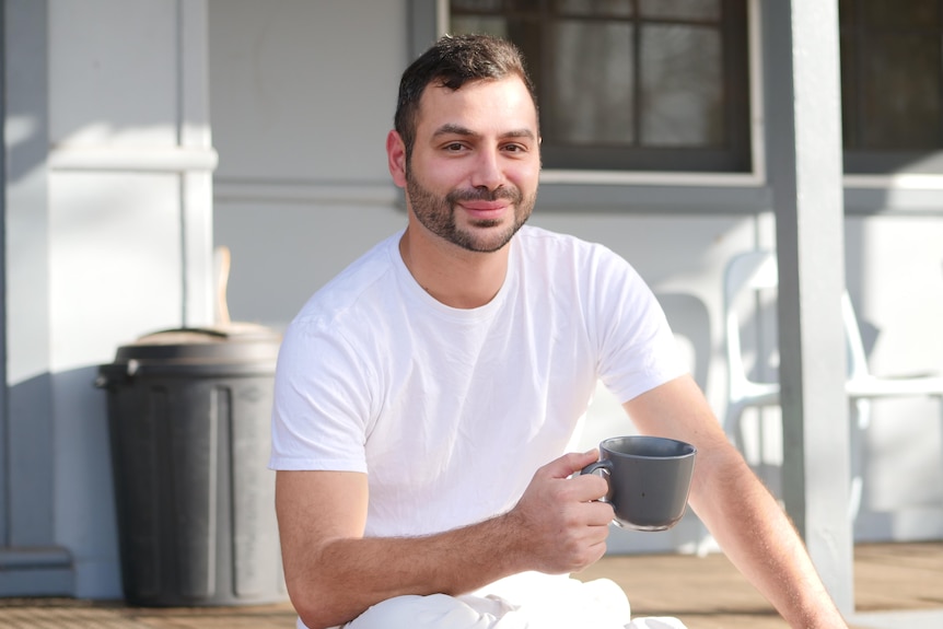 A bacpacker sits on a step with a coffee