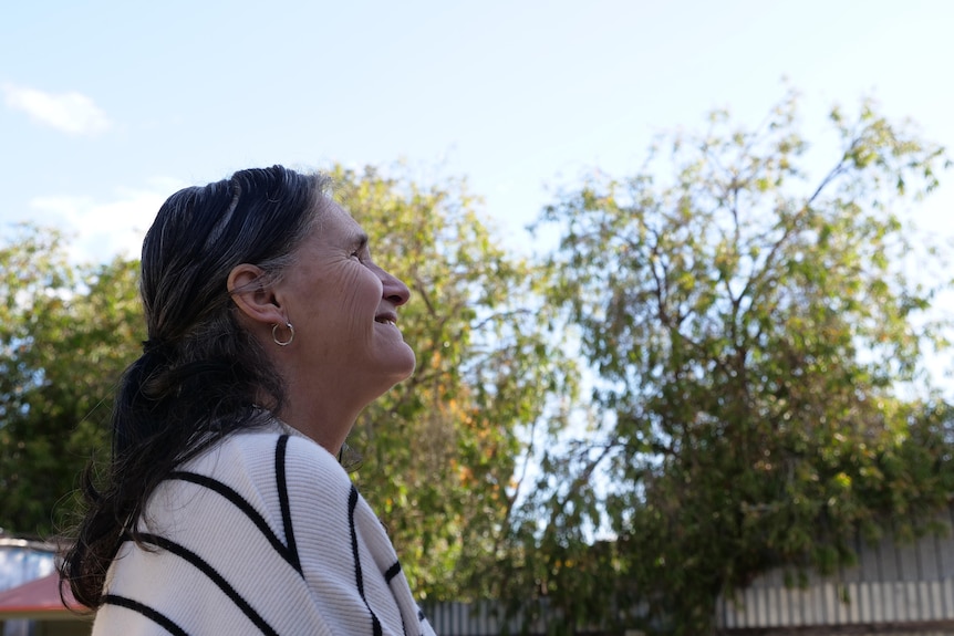 A woman smiles as she looks off into the distance, into the blue sky. She is wearing a white and black striped jumped.