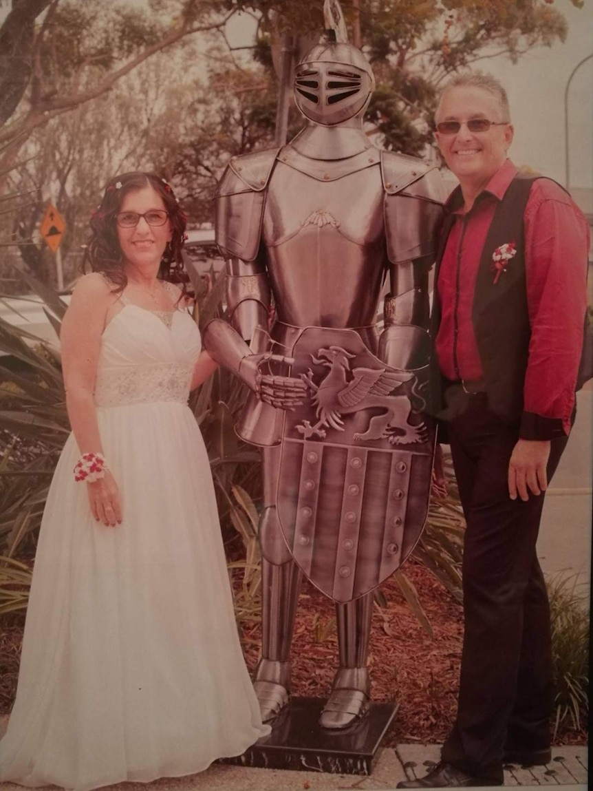 A framed wedding photo of a bride and groom posing with a silver suit of armour.