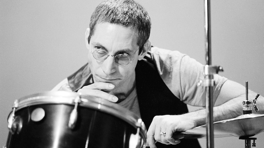 Rolling Stones drummer Charlie Watts, with cropped hair and glasses, leans on his drum kit
