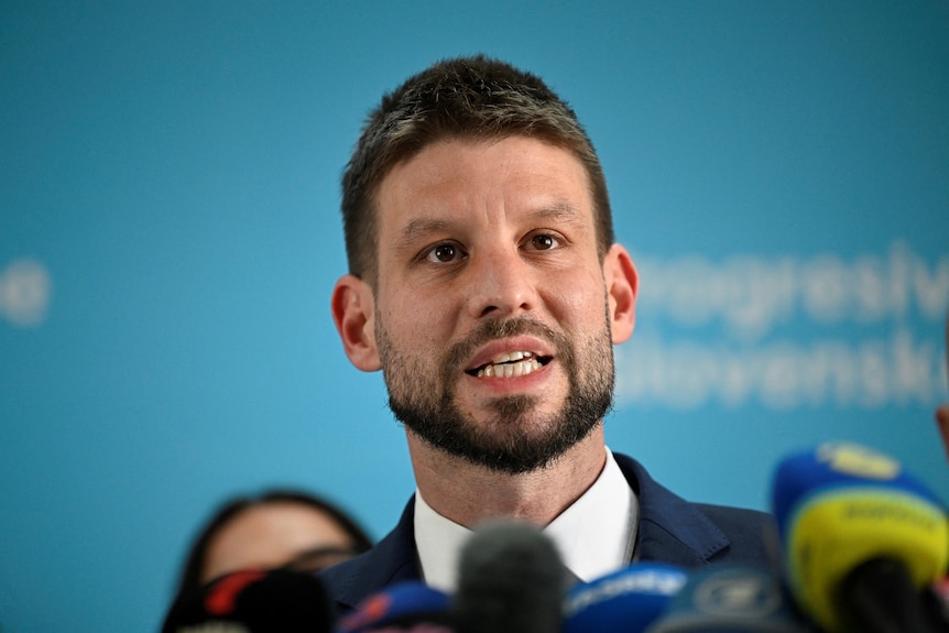 Michal Simecka stands speaking in front of a number of microphones.