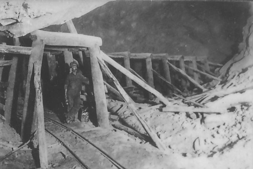 A black and white image of a mine worker standing near a wooden mineshaft frame