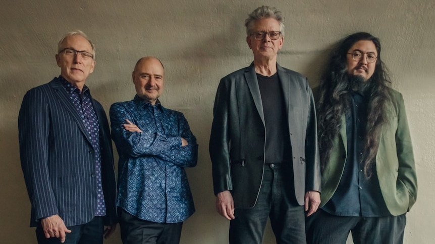Members of the Kronos Quartet stand against a beige wall