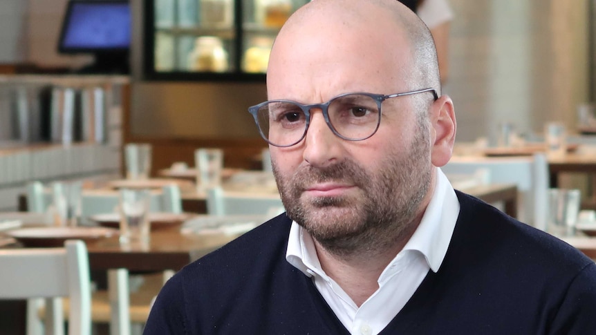 George Calombaris wears a white shirt and navy jumper