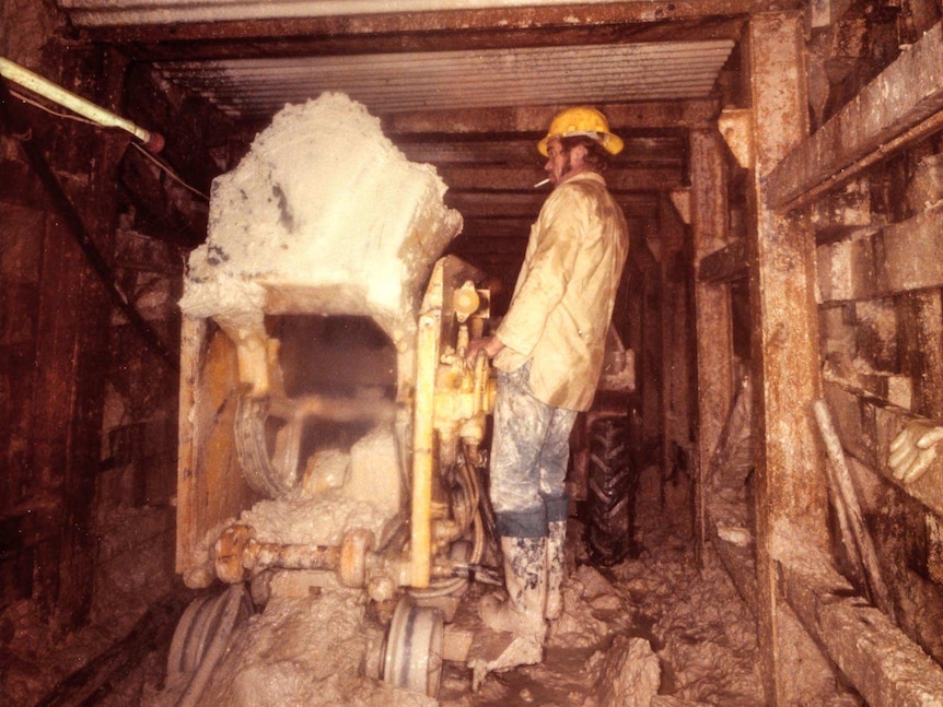 A man smokes a cigarette while working a machine in an underground tunnel