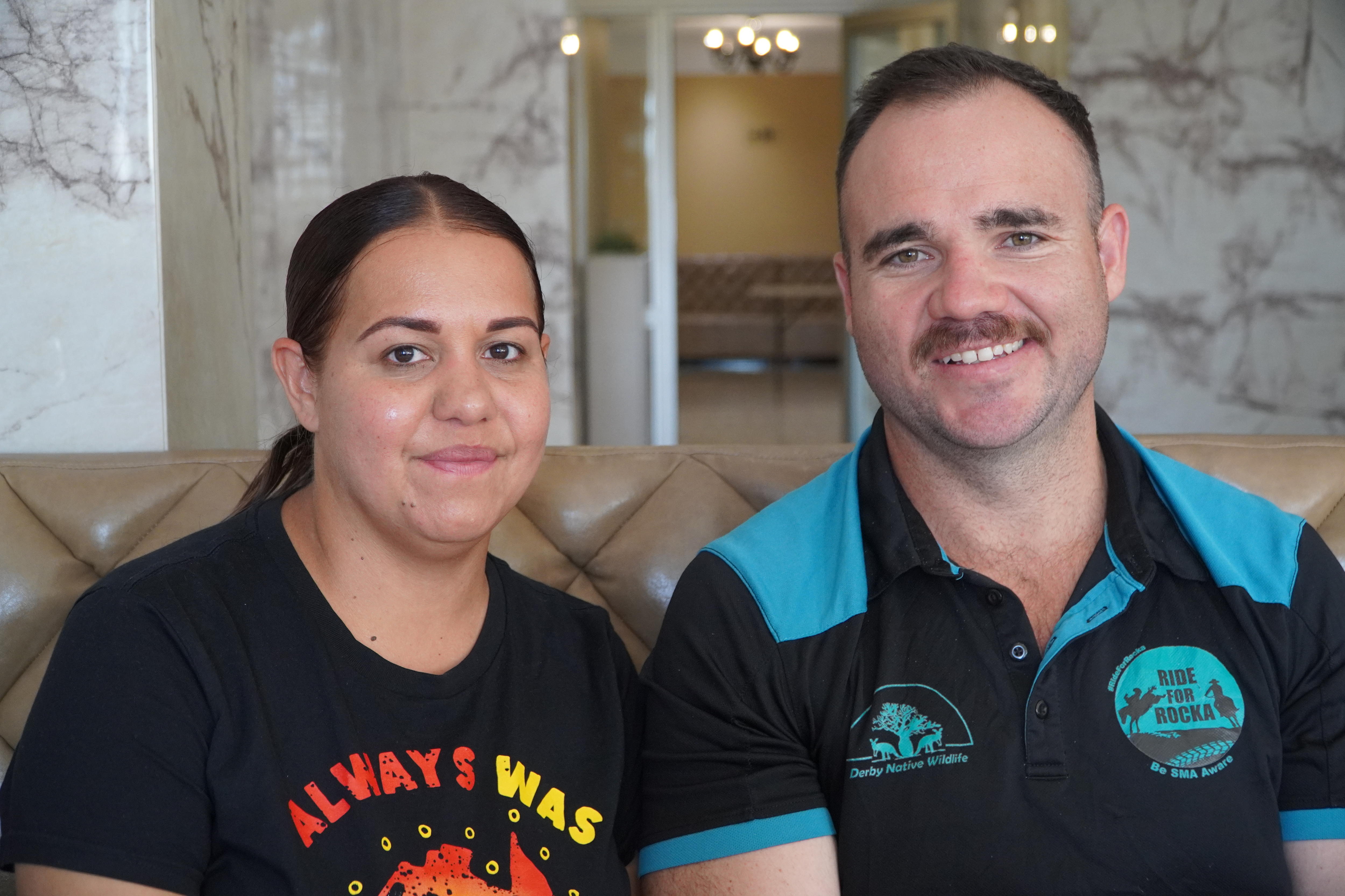 Um jovem casal senta-se no sofá e sorri para a câmera.