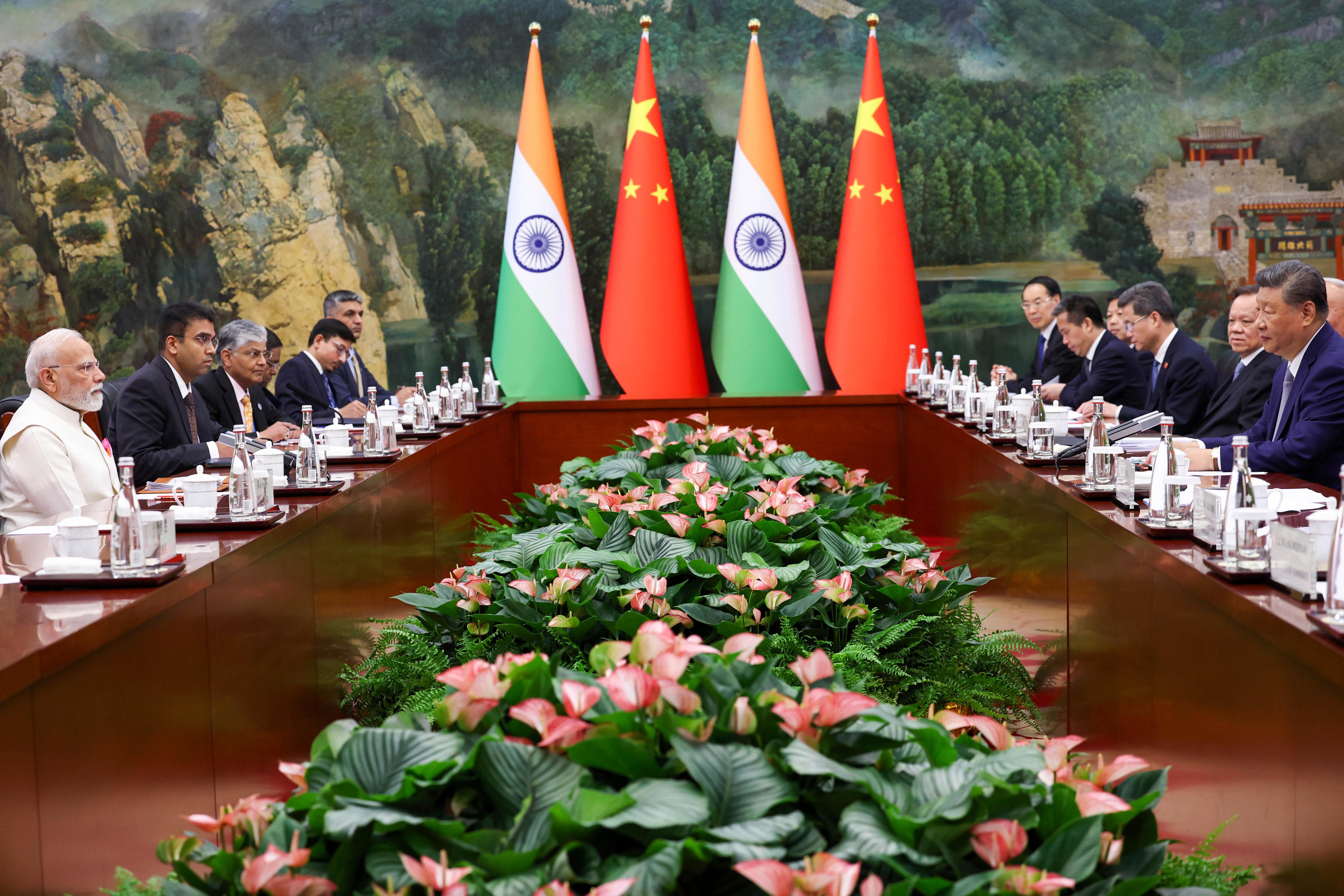 men seated with tea kettles and cups on either side of wooden long table. four flags in the middle on short edge. flowers in ce