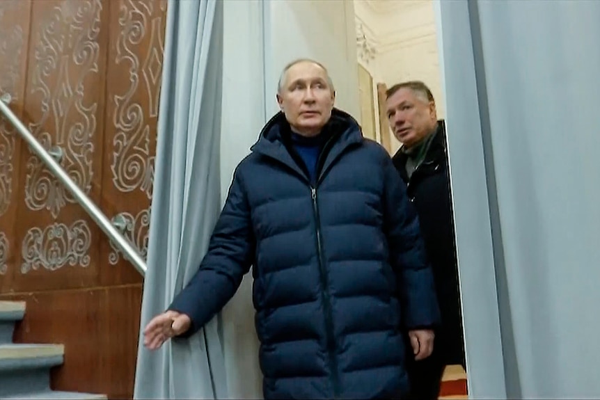 Vladimir Putin pushes open a blue curtain with a middle-aged man behind him