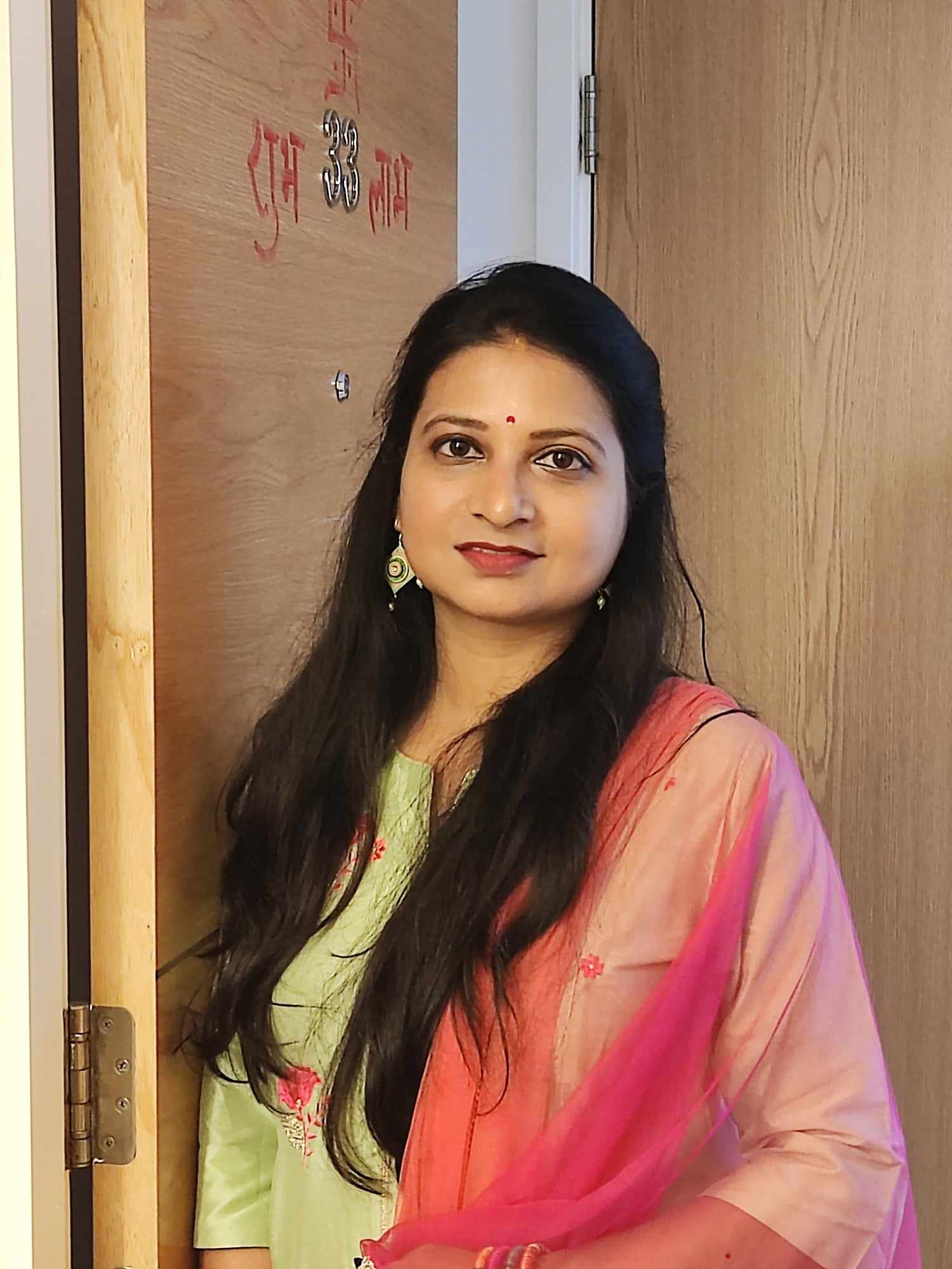 A woman with long black hair, dressed in traditional Indian clothing smiling at the camera