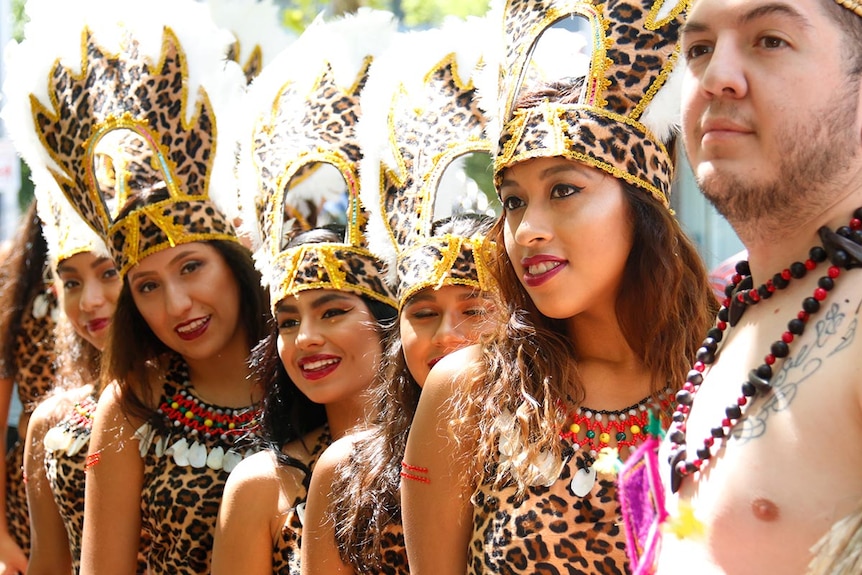 A group of women in elaborate animal skin costumes ad feathered head dresses stand together.