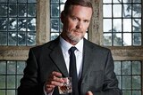 Man in dark suit holds glass of whisky