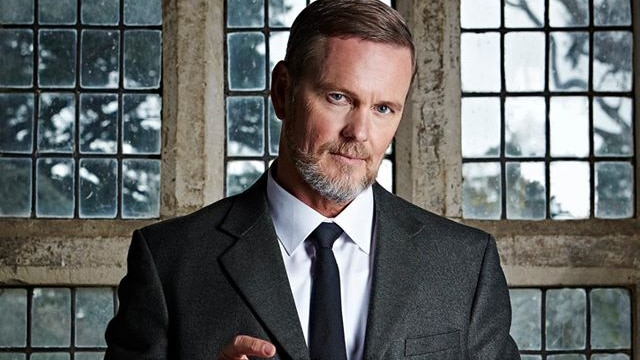 Craig McLachlan in a dark suit holding a glass of whisky