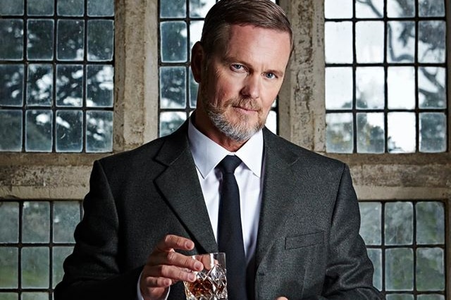 Man in dark suit holds glass of whisky