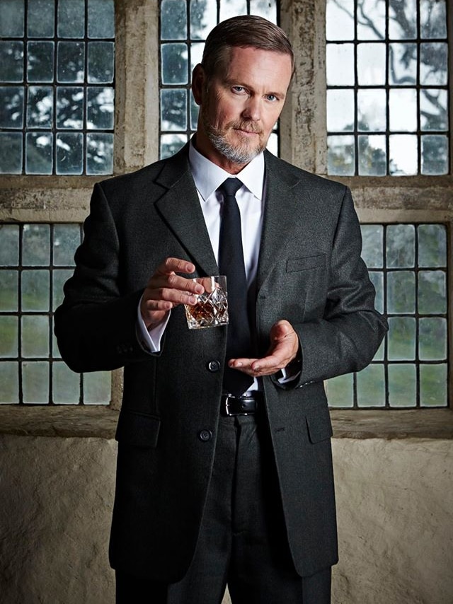 Man in dark suit holds glass of whisky