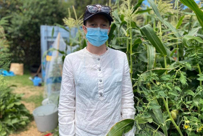 A woman in a face mask stands in a veggie patch garden.