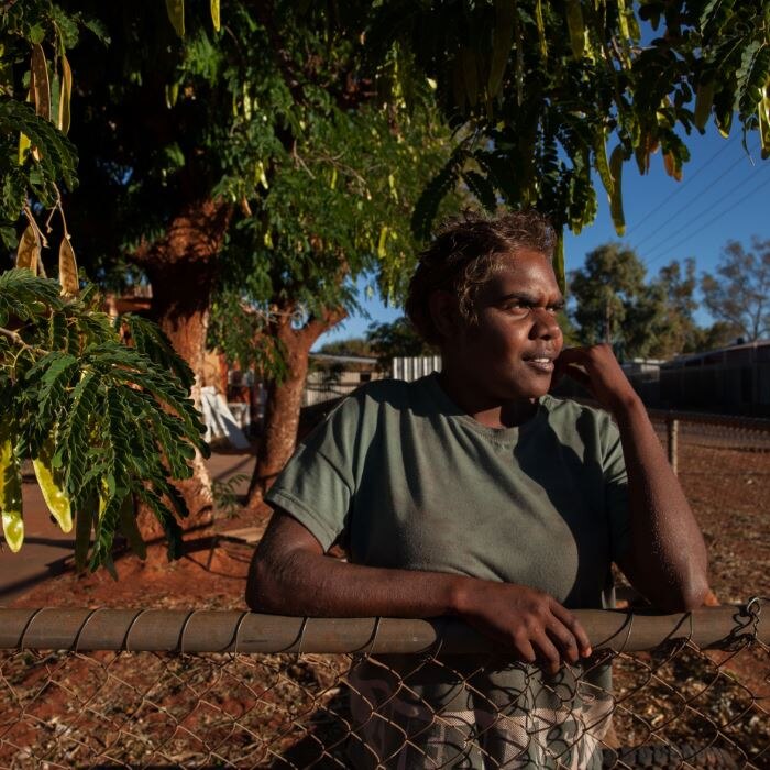 Indigenous woman Letisha West leans on a garden fence in front of a tree