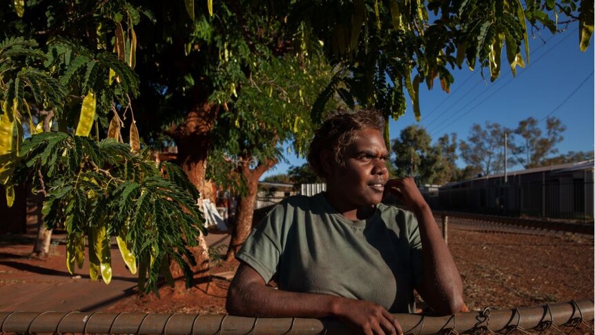 Indigenous woman Letisha West leans on a garden fence in front of a tree