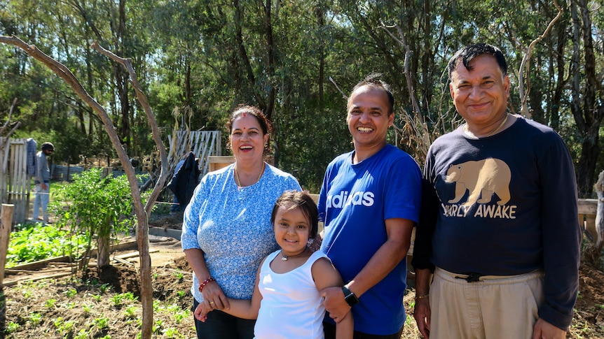 Tikal stands with his daughter and parents in the community farm, all four are smiling and crops can be seen in the background.