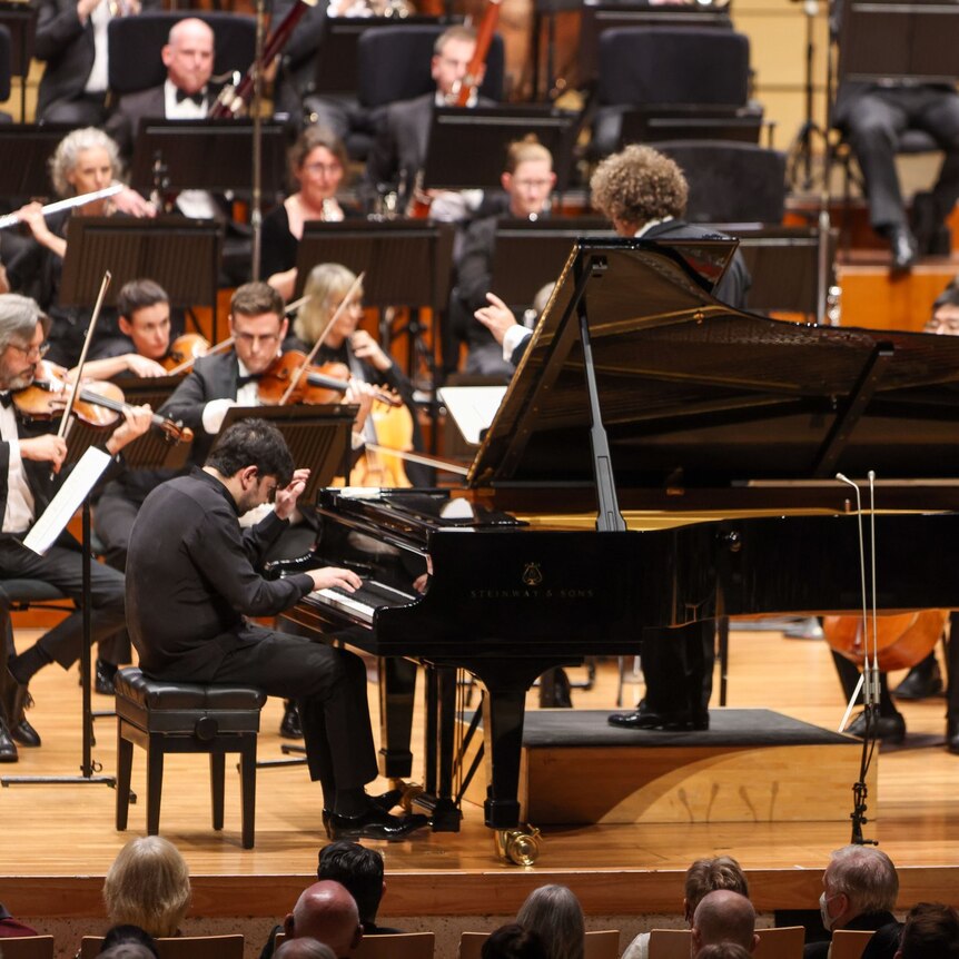 Pianist Behzod Abduraimov playing piano on stage with the queensland symphony orchestra.