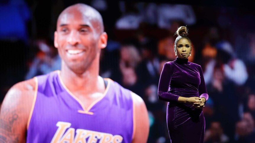 A female singer stands in front of a video montage of Kobe Bryant.