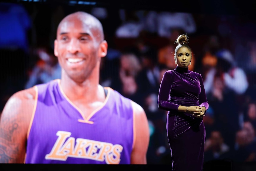 A female singer stands in front of a video montage of Kobe Bryant.