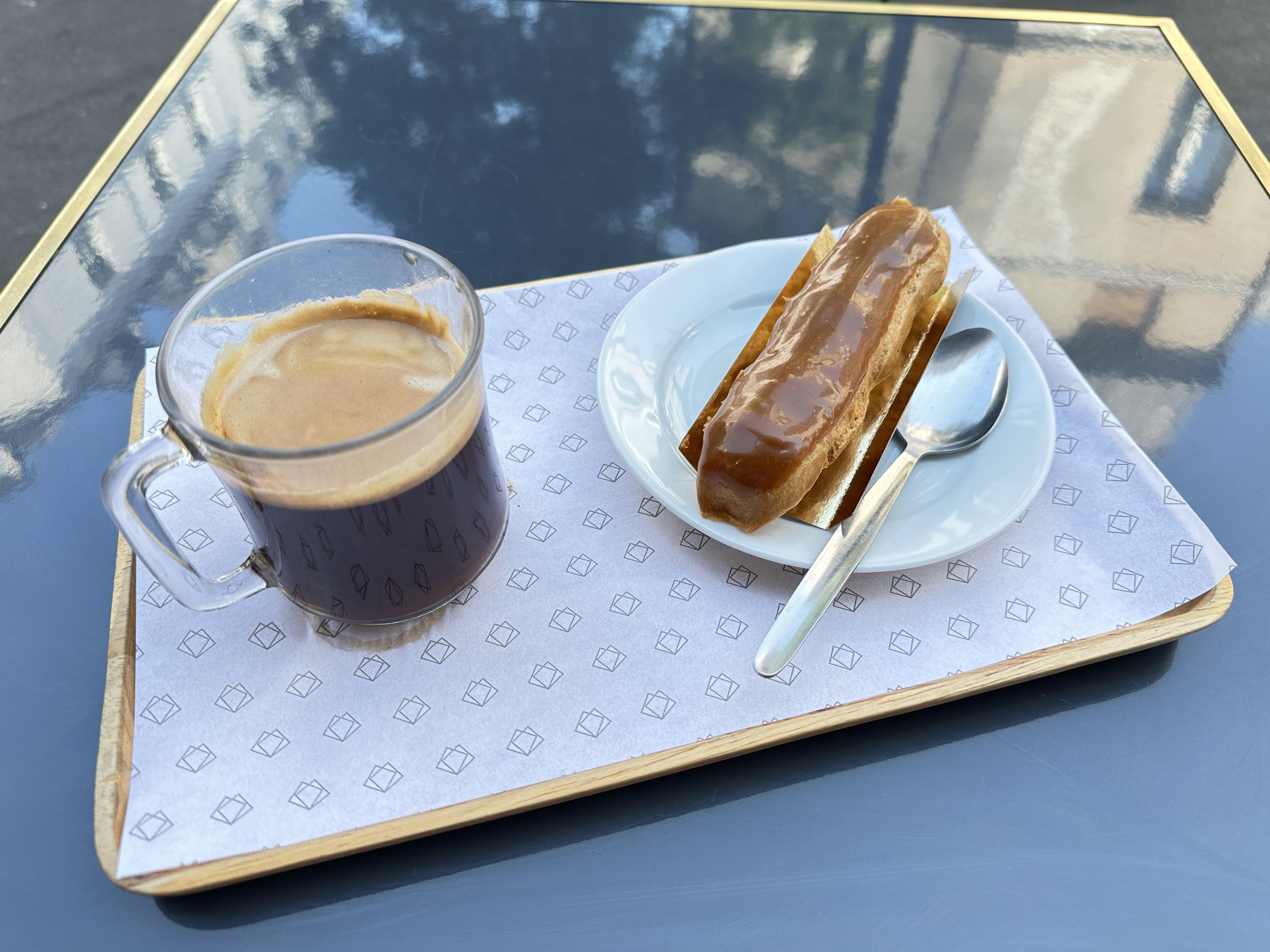 A coffee and eclair on a tray on an outdoor table in Paris.
