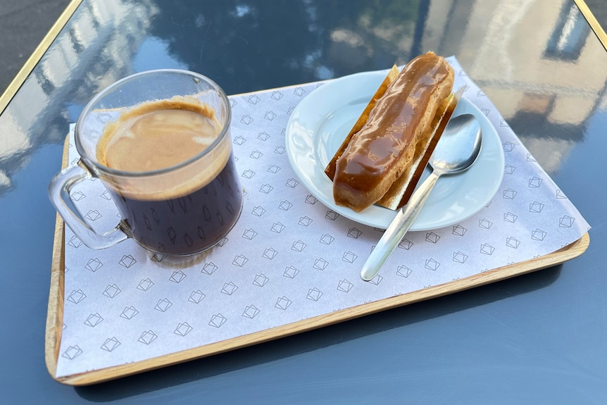 A coffee and eclair on a tray on an outdoor table in Paris.