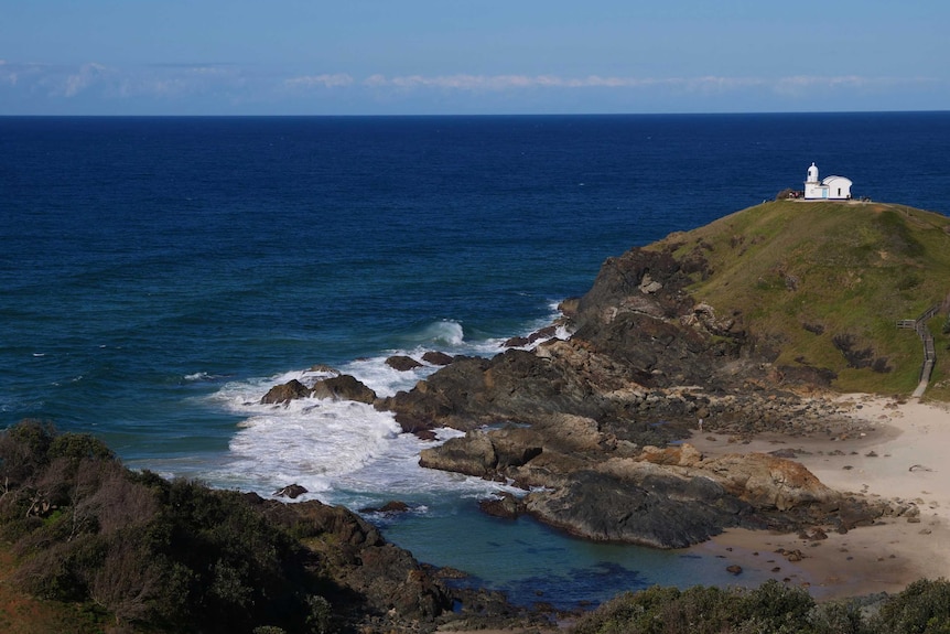 A green headland surrounded by ocean, with a lighthouse in the distance.