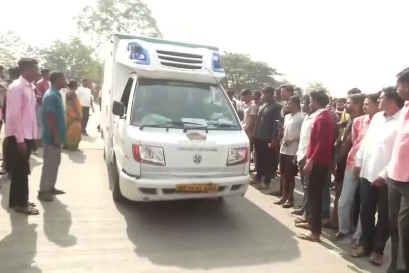 People stand alongside an ambulance on a dirt road 