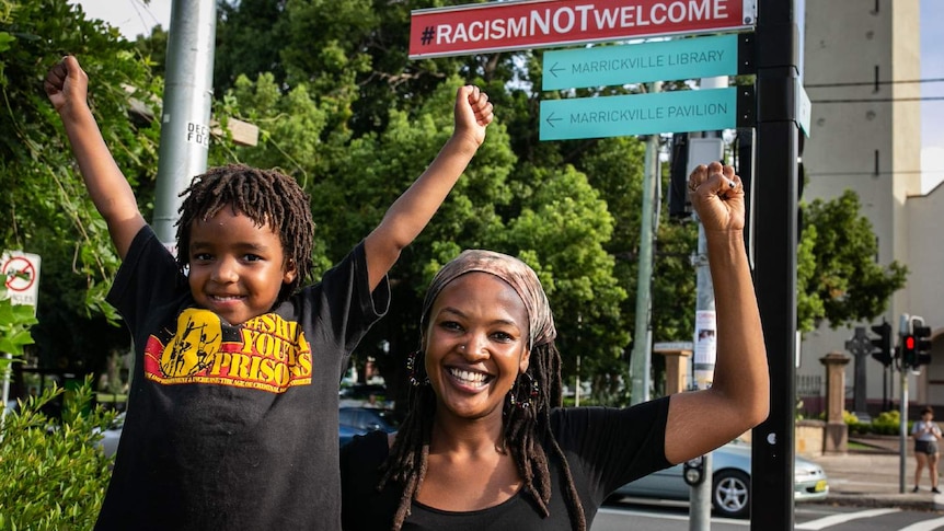 A woman and a girl stand below a road sign